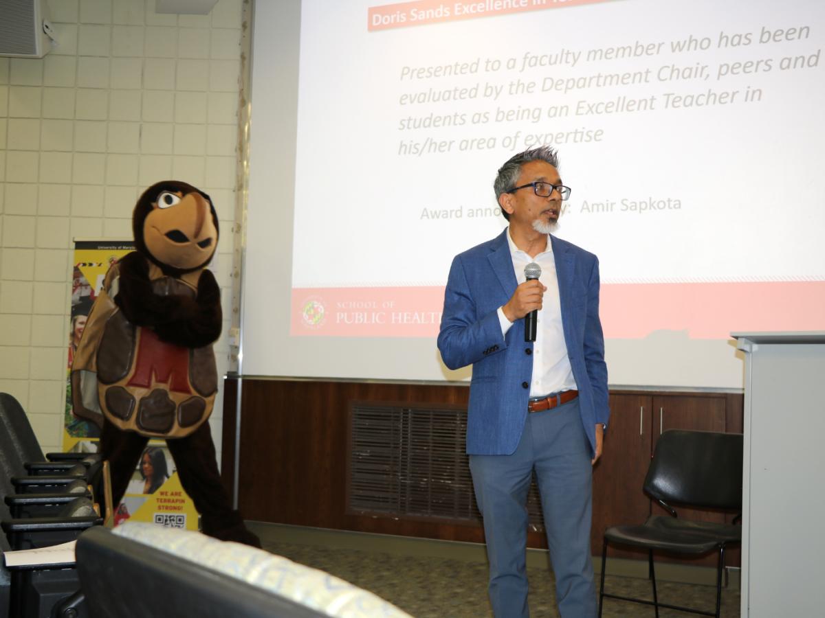 faculty member presenting an award with Testudo mascot in background