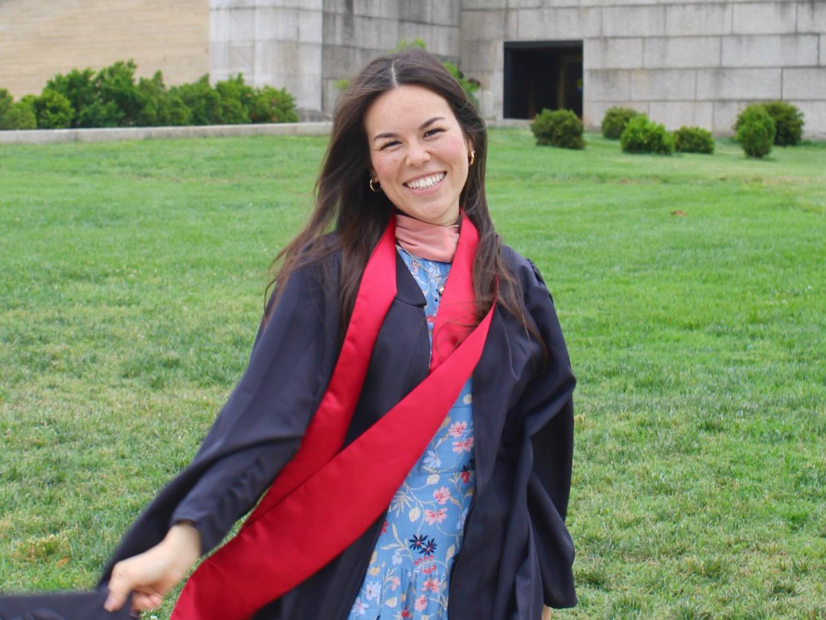 Woman with long brown hair, posing in graduation attire