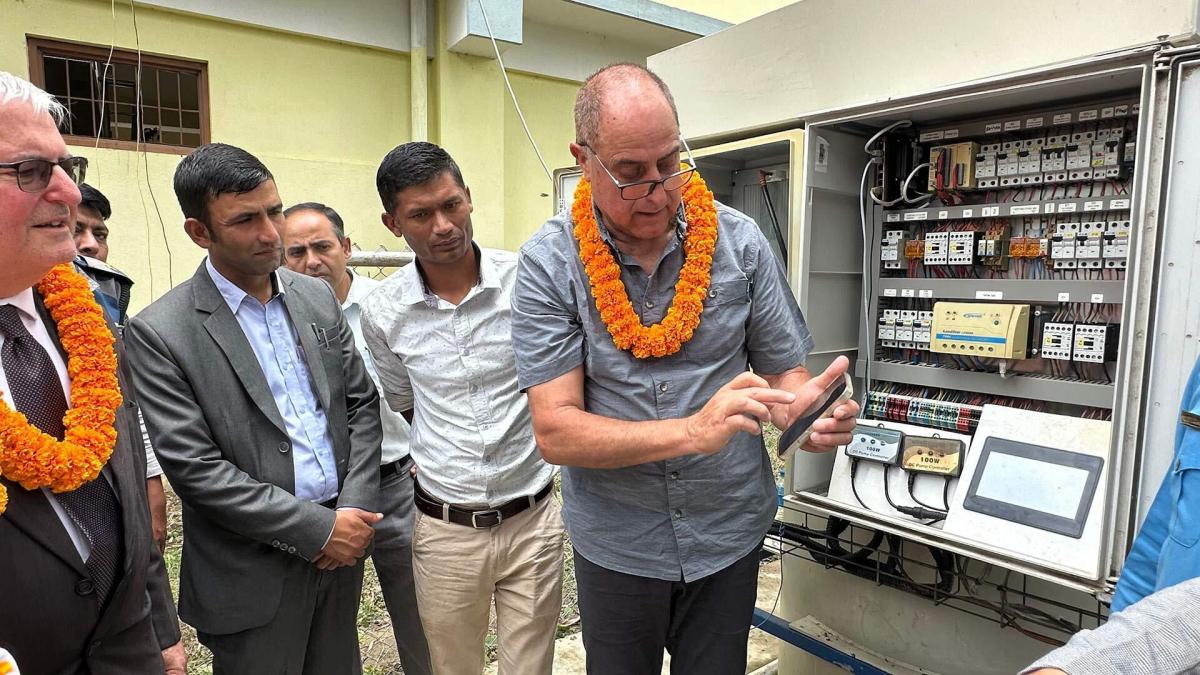 Group of American, Nepali and Israeli men stand in front of a machine that demonstrates the remote monitoring system that uses a cellphone-based app to provide real-time data