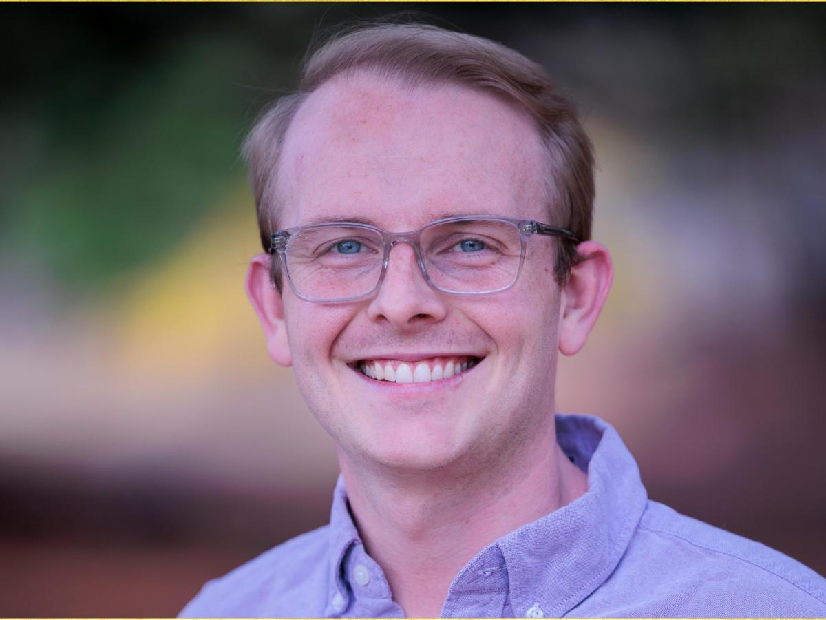 White man with wire rimmed glasses, short brown hair, lavender button-down smiling