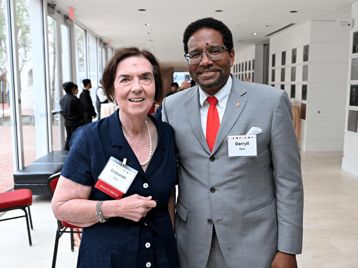 Older white woman in navy suit dress poses with older Black man president of the university in a grey suit with red tie