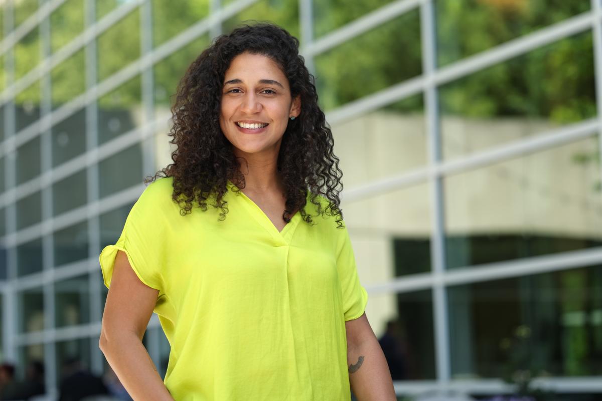 Woman wearing a yellow shirt with hand on hip smiling at camera.
