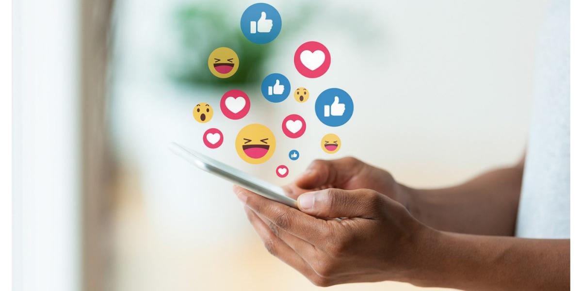 two hands hold smart phone with emojis popping up and hovering above the screen