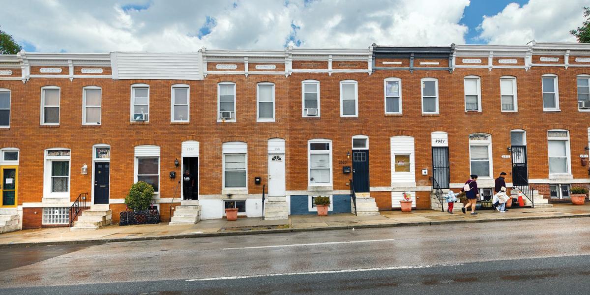 Row of brick homes on a Baltimore city street with clouds above and a tarmac road in front
