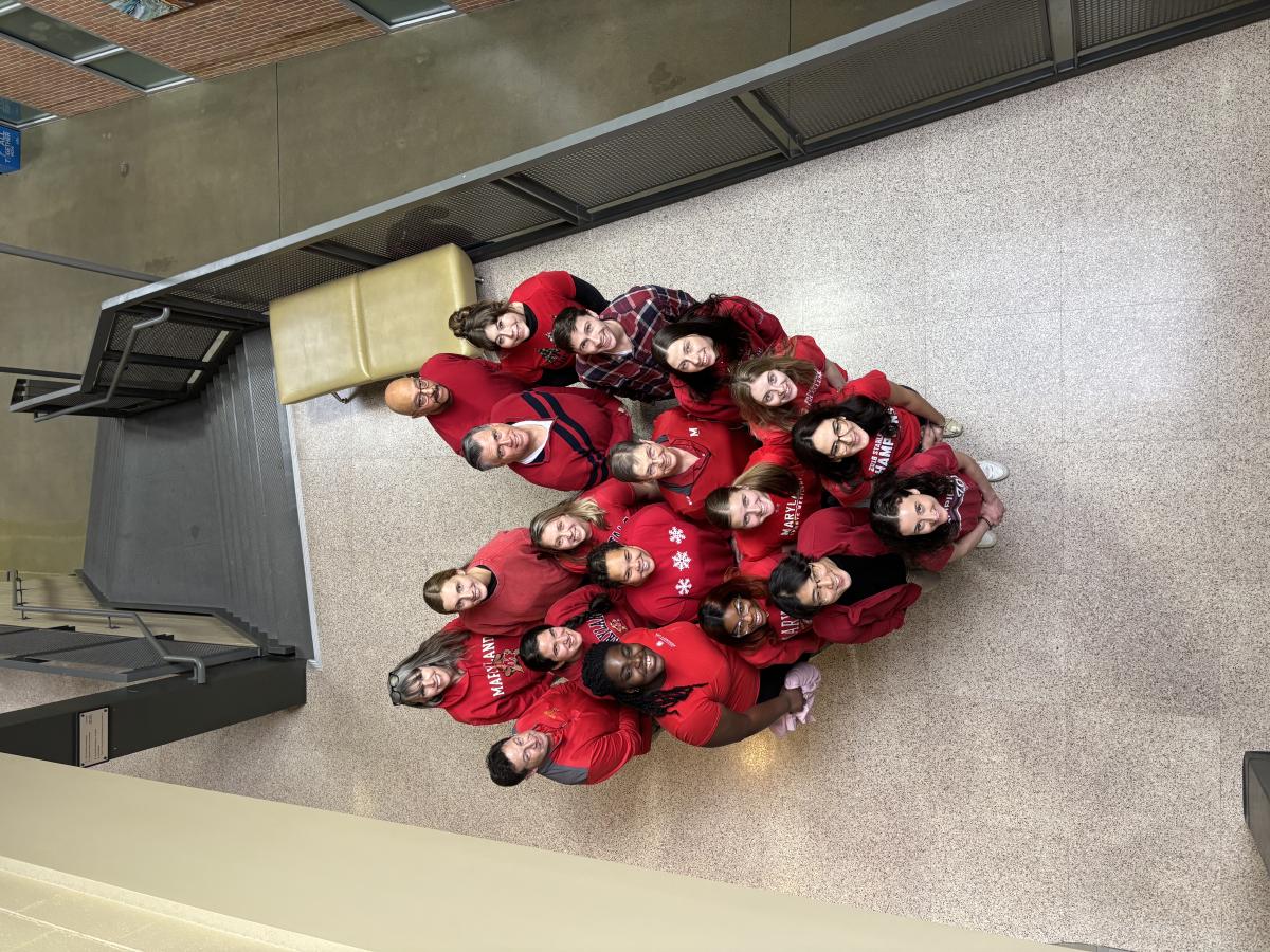 Group of adults wearing red shirts standing together in the shape of a heart.