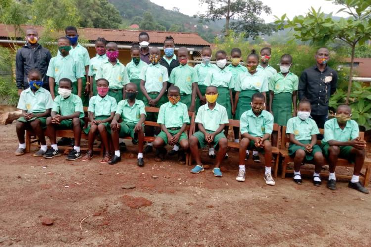 Two rows of children dressed in green school uniforms and wearing COVID-19 face coverings at the Abigail D. Butscher Primary School in Sierra Leone (Photo credit, M. Tholley.)