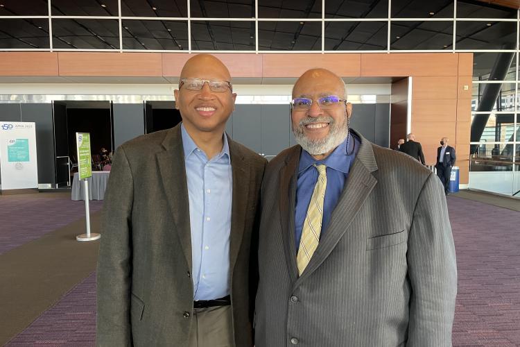 Sacoby Wilson, wearing a blue shirt and grey suit jacket, stands to the left of Dr. Georges Benjamin, executive director of APHA, who is wearing a blue shirt, yellow tie and grey suit jacket.