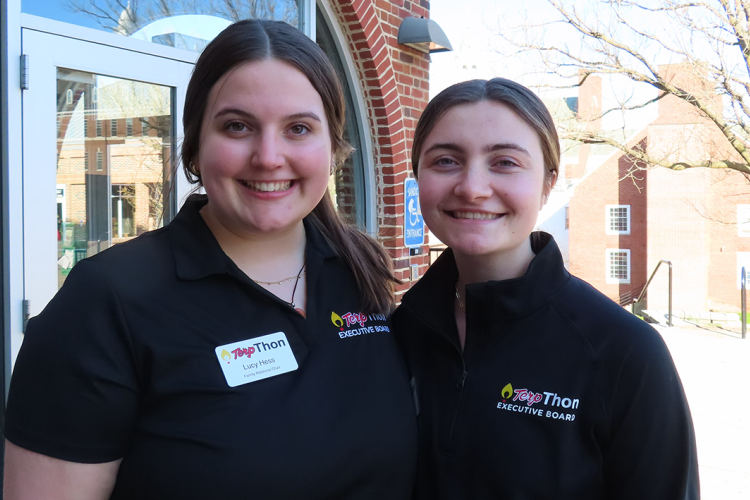 Two young women stand next to each other outside, wearing black shirts.
