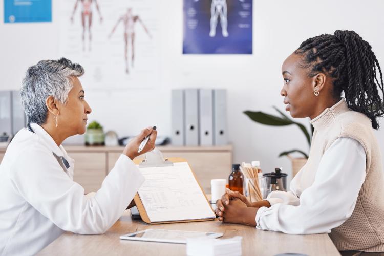 an Asian woman doctor speaks to a black woman patient