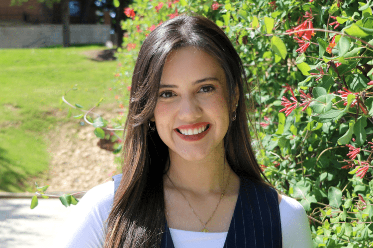 student graduation speaker smiles to camera, outside in front of flowers and grass
