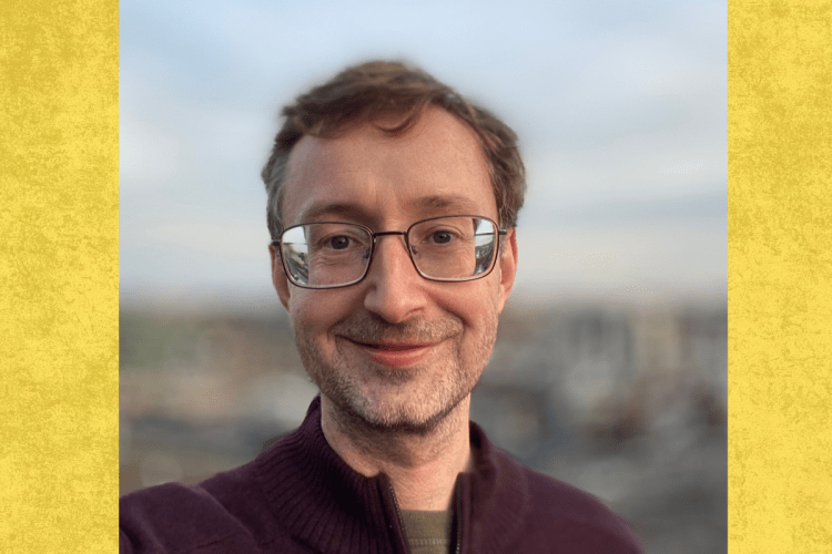 Professor smiles to camera with blurry cityscape behind him 