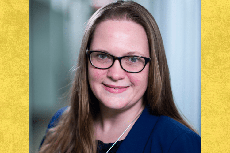 professor woman wearing navy top and glasses smiles to camera