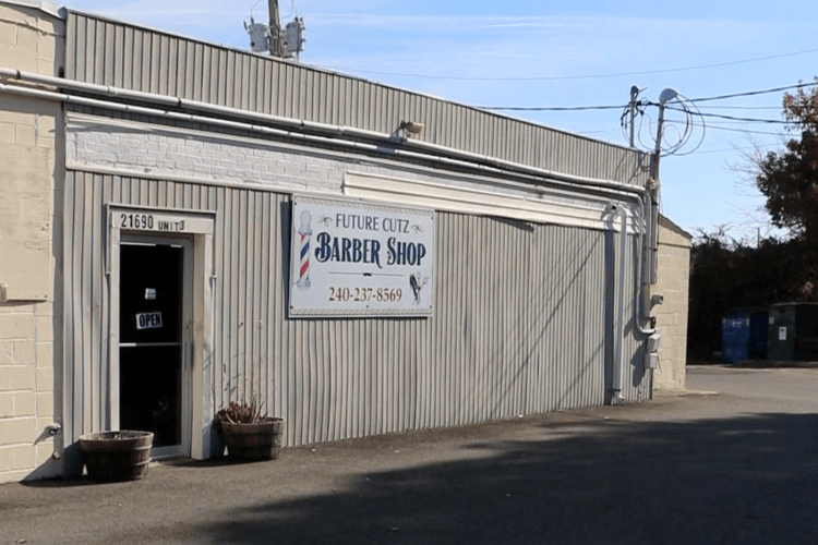 Outside of a barber's shop with sign, FUTURE CUTZ, with empty concrete lot in front