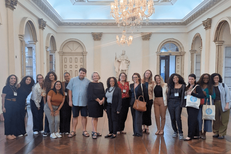 Group of students and faculty pose in a grand high ceilinged room with a chandelier