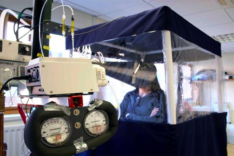 woman in blue top and long dark hair sits inside the Gesundheit II machine that measures pathogens in exhaled breath. 
