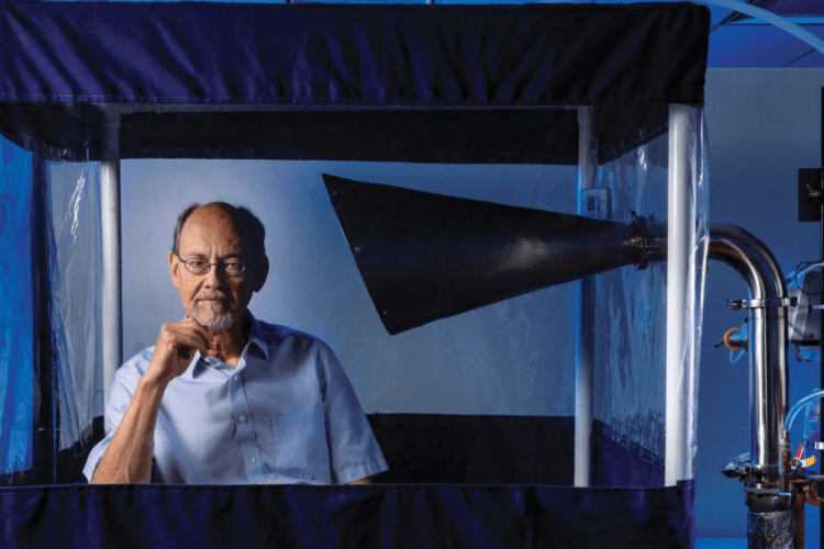 Professor sits inside his invention, the Gesundheit machine, looking at camera with hand to his chin