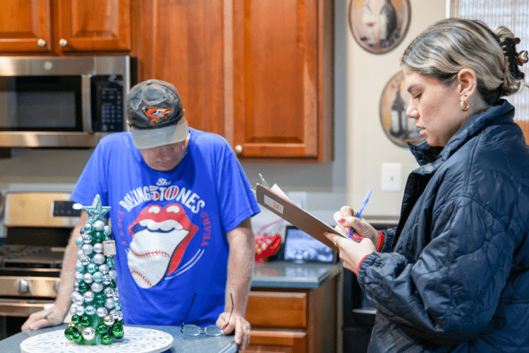 Researcher takes notes from homeowner who looks down at the table in the kitchen