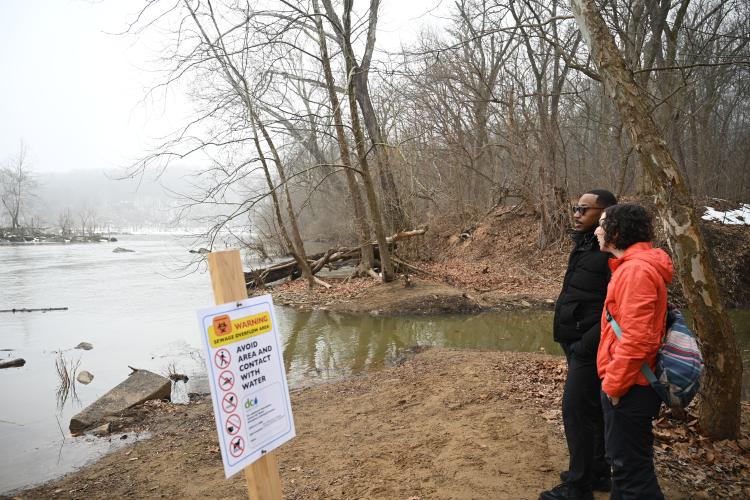 Two UMD professors talk at the site of Potomac River sewage spill with sign warning of health hazards