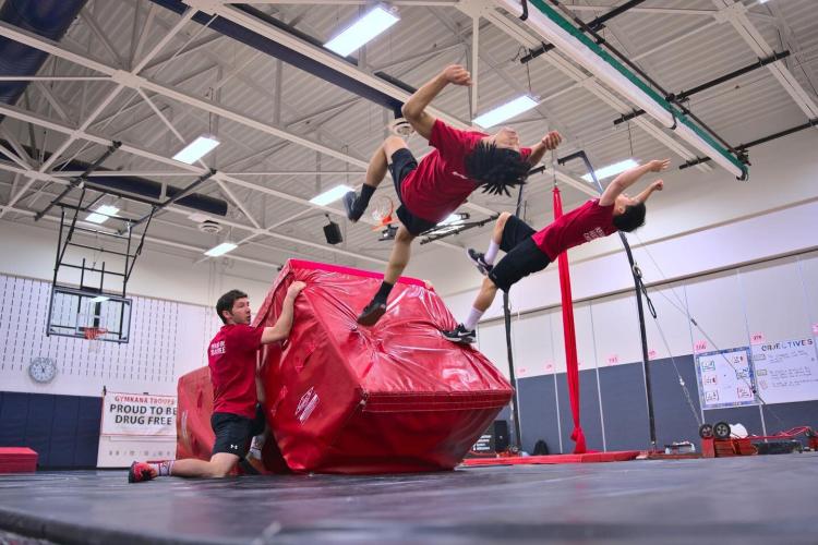 Two kids tumble in the air from a practice block with a coach watching them