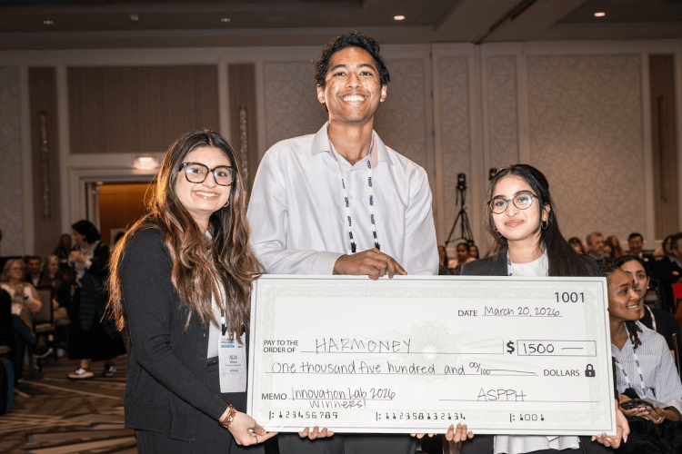 Three students smile at the camera, holding a big check award