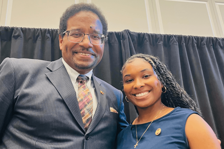 Black man in suit and young black student woman in teal top smile to camera