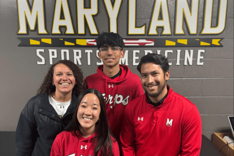 Four Maryland staff pose in sweatshirts in front of MARYLAND SPORT MEDICINE on wall behind them