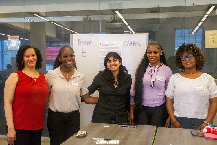GRoup of 4 students with a professional stand in front of a white. board