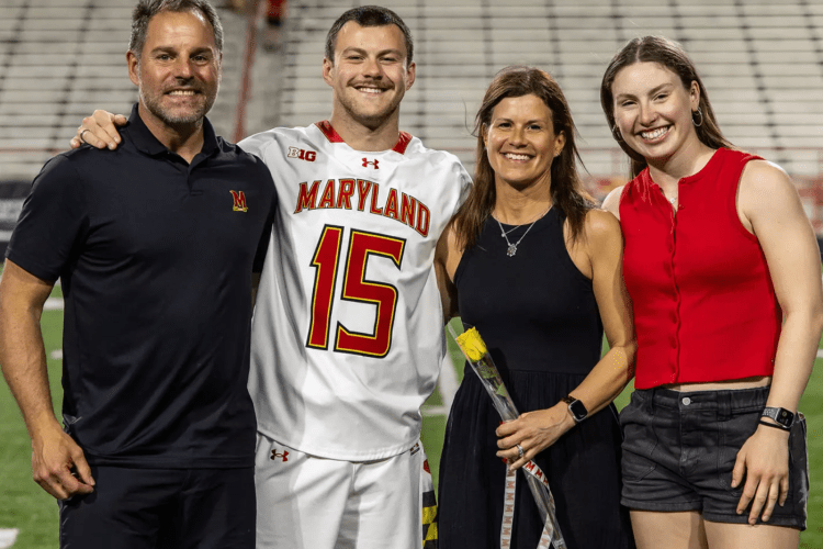 Young male athlete in Maryland athletic gear poses with mother, father, sister, with stadium bleachers in background