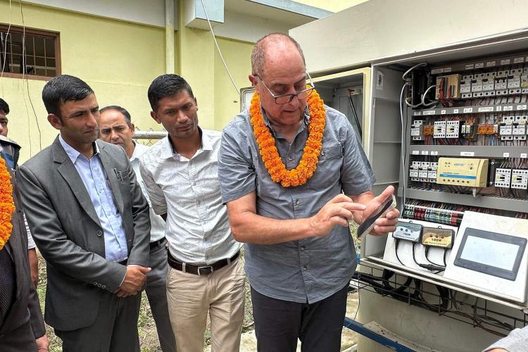 Group of American, Nepali and Israeli men stand in front of a machine that demonstrates the remote monitoring system that uses a cellphone-based app to provide real-time data