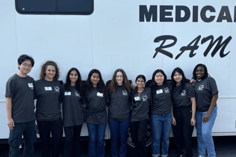 Group of students in matching dark blue tshirts stand in front of the RAM vehicle