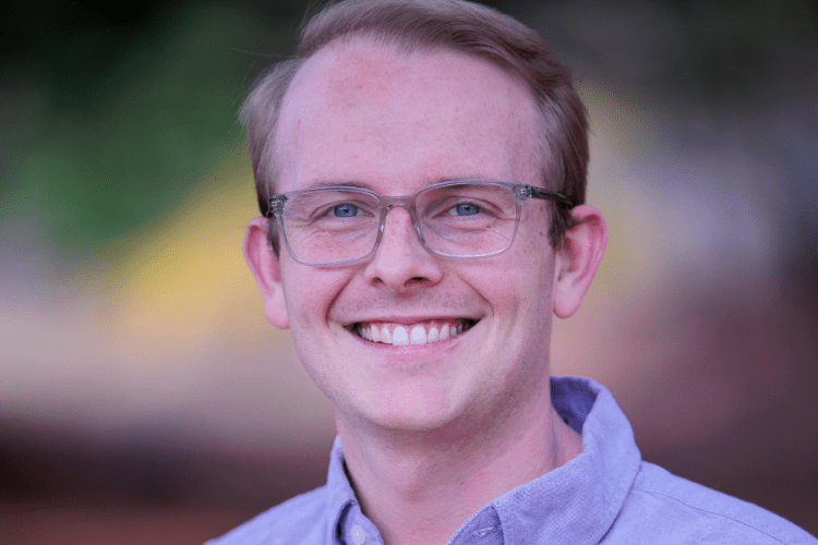 White man with wire rimmed glasses, short brown hair, lavender button-down smiling