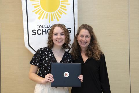Student holds an award certificate and smiles at the camera while standing next to her faculty advisor.