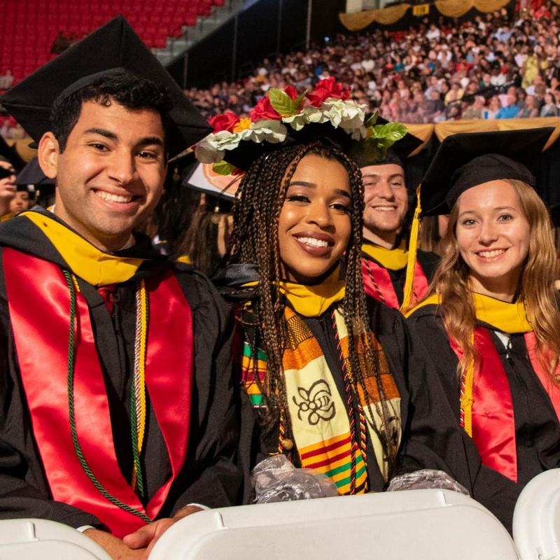 Students wearing caps and gowns at a commencement ceremony smiling at camera