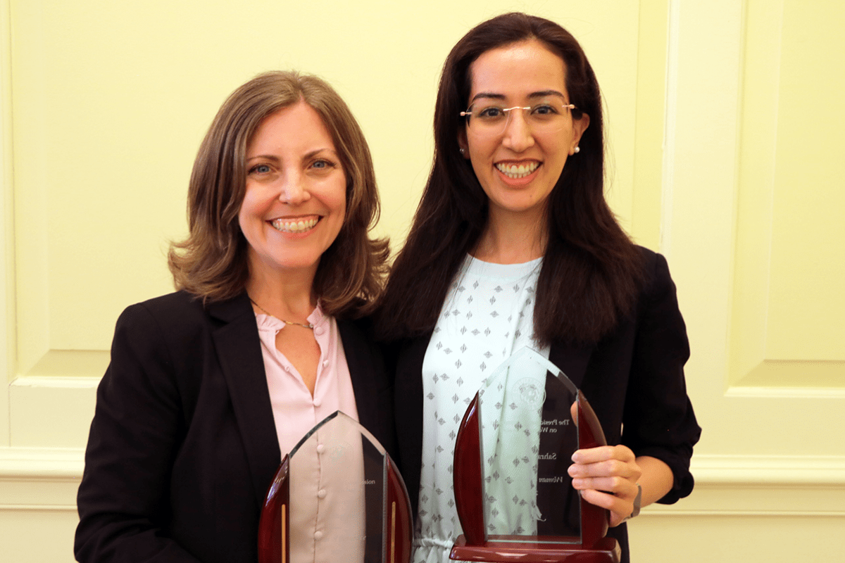 Professor Amy Sapkota and Sahra Ibrahimi stand next to each other holding glass-like awards.