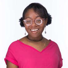 Dark skinned woman with glasses wearing a pink shirt