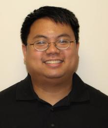 Man with short dark hair smiling while wearing glasses