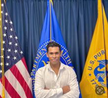 Man with short dark hair standing in front of flags