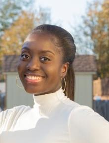 Dark skinned woman smiling at camera with hair pulled back in pony tail