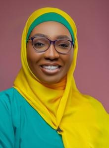 Woman smiling at camera wearing a yellow headscarf and glasses