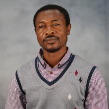 Gabriel Dogbania is wearing a gray vest on top of blue, white and red gingham patterned shirt
