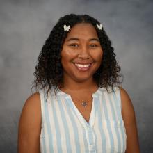 Mya Smith is whearing a blue and white striped blouse and smiling the 1:1 headshot
