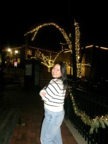 Woman with white and black striped shirt looking over her shoulder at the camera with trees lit up in the background