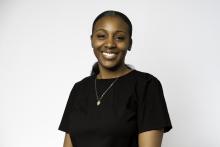 Woman with black short sleeved shirt and gold necklace smiling at the camera with a white background