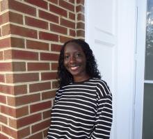 Woman with black and white striped shirt against a brick background smiling at the camera
