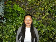 Woman with white shirt and grey sweater smiling at the camera with a live greenery background