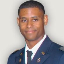 Black man wearing military suit and short hair smiles to camera