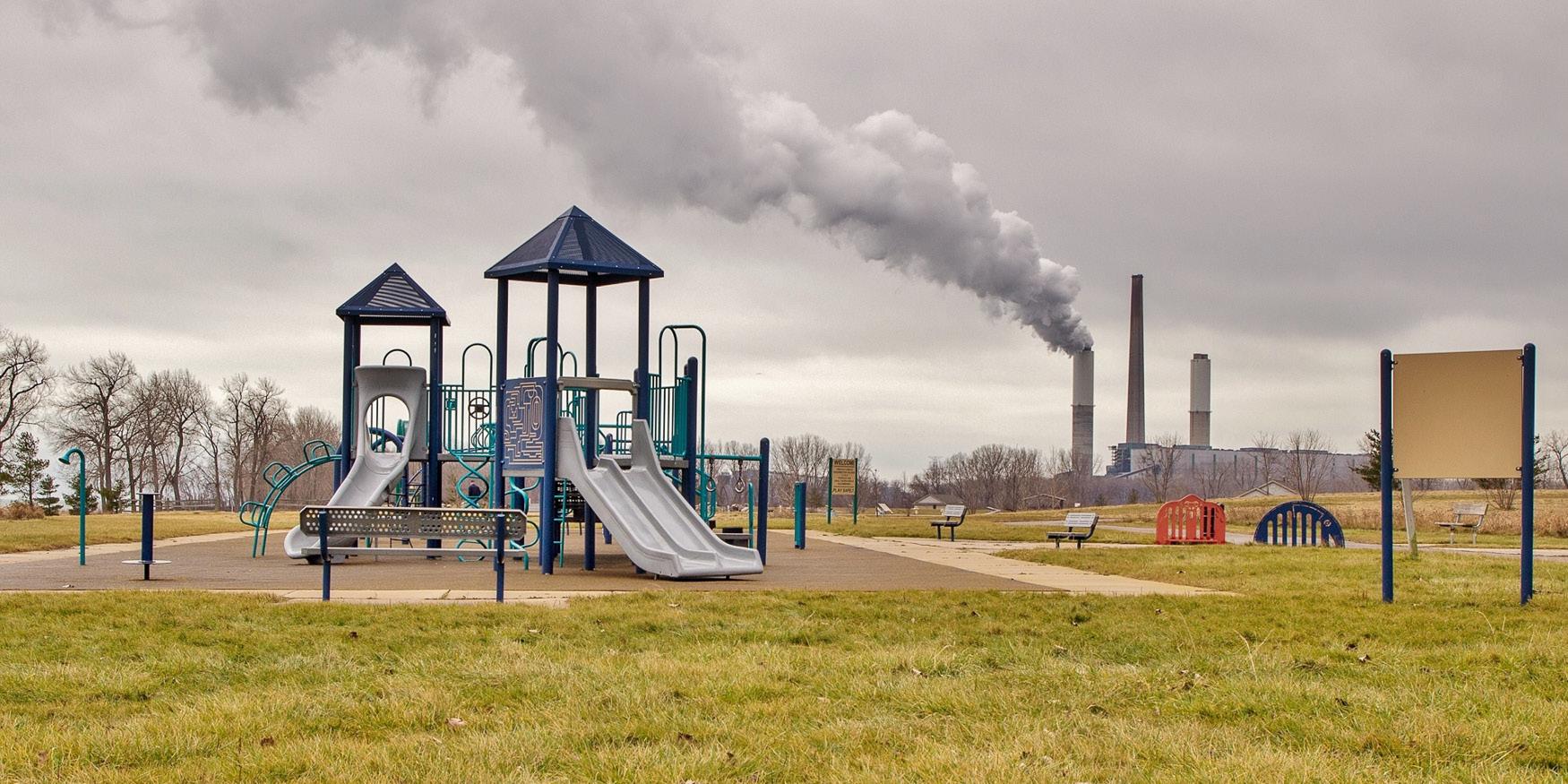 Children's playground with a smokestack billowing smoke in the background.
