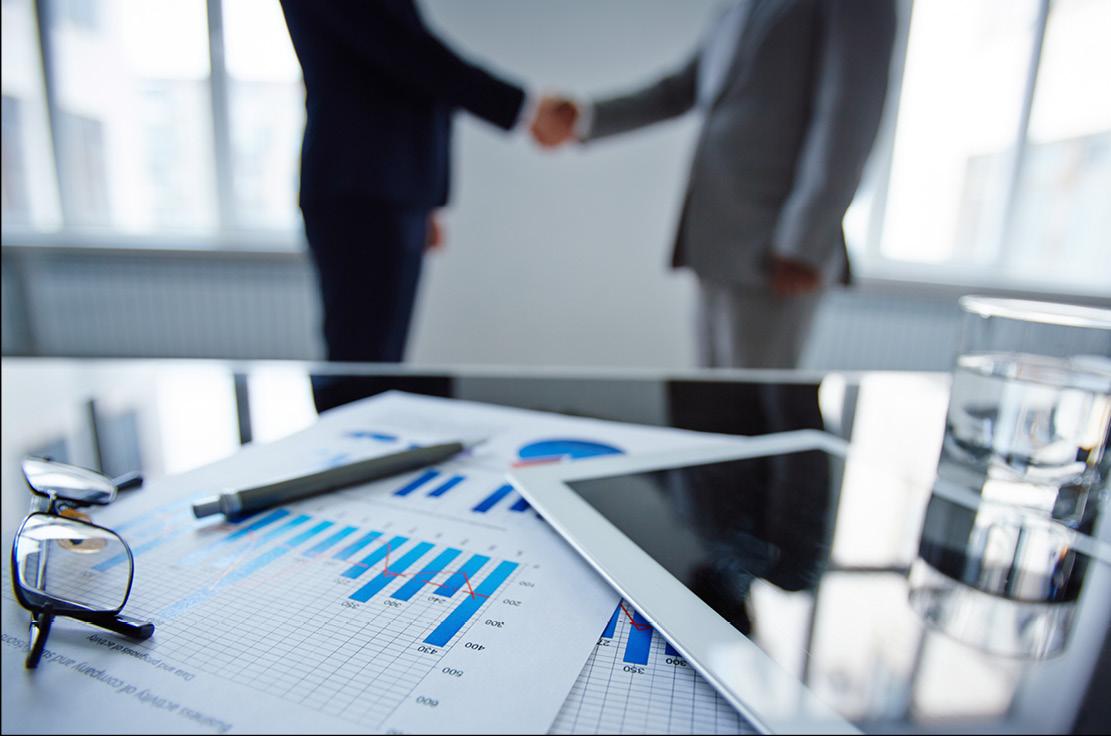 Two people handshaking next to desk with graph charts