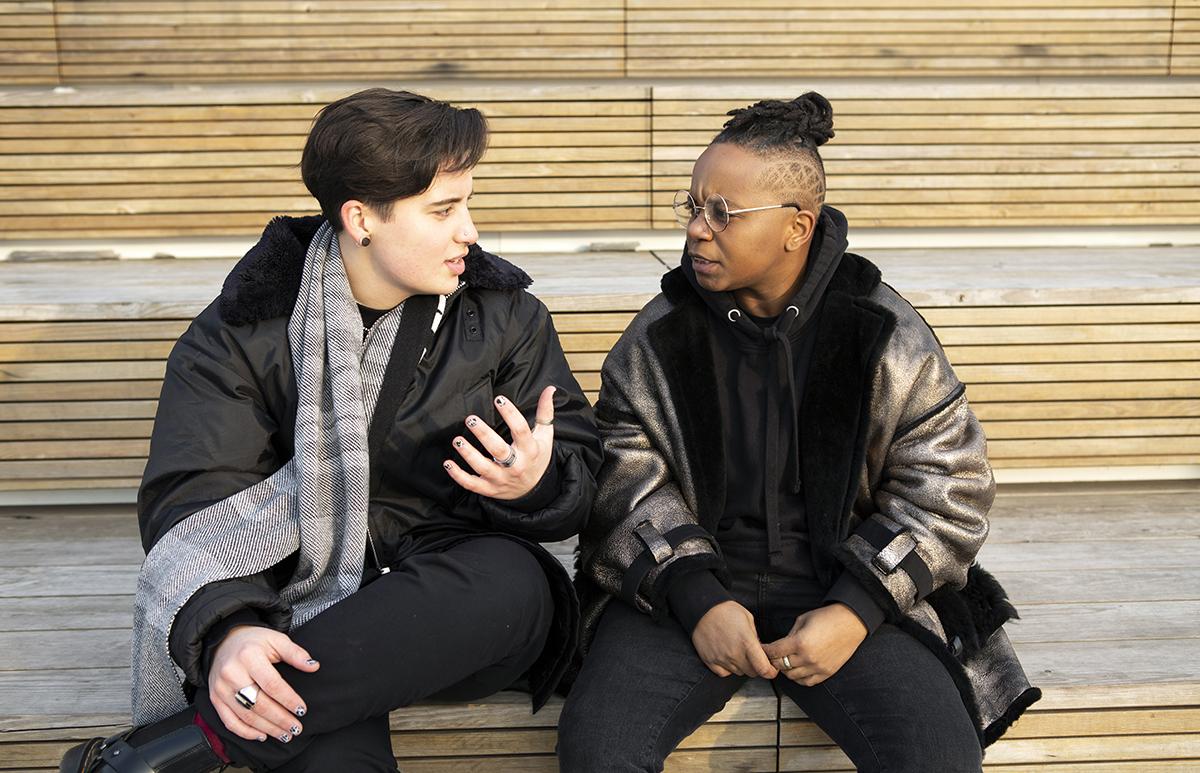 Two transmasculine people talking outside 