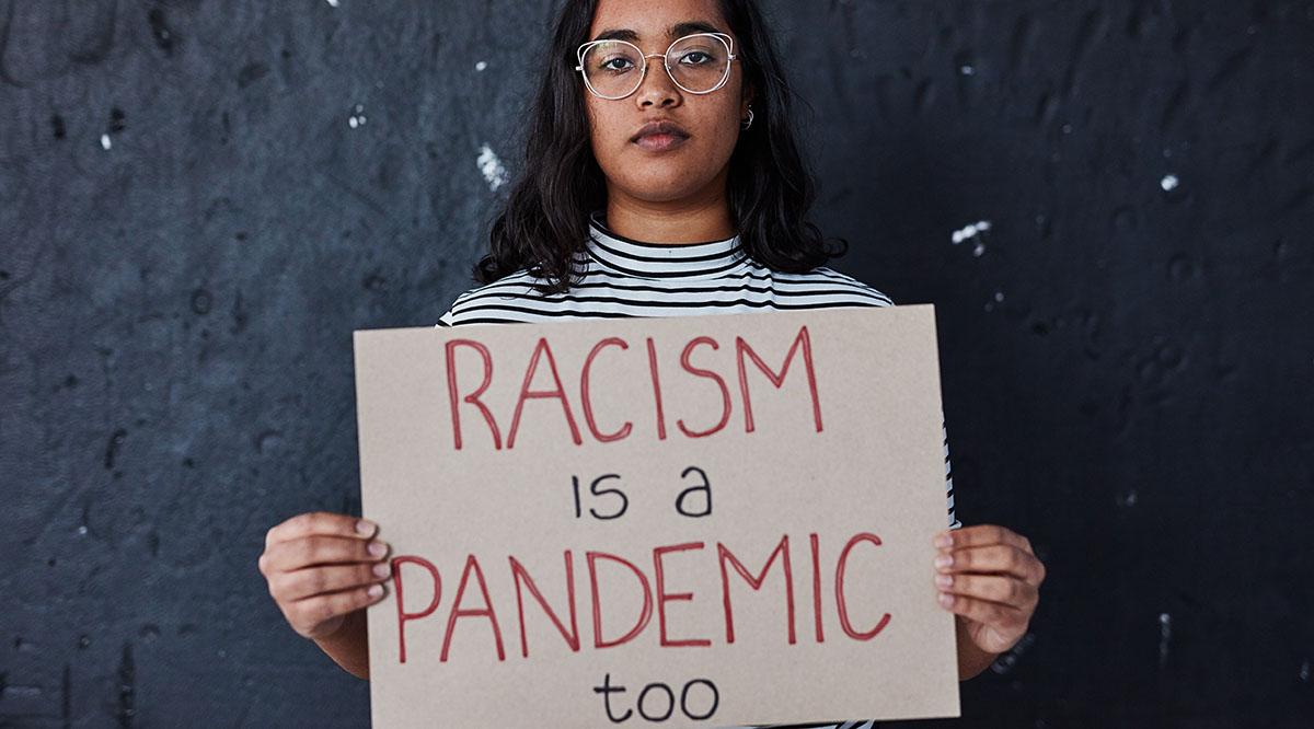 Woman holding a sign that reads "Racism is a pandemic too"